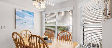 A dining area with a wooden table and chairs, a ceiling fan, and a painting on the wall.