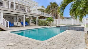 A swimming pool with a white deck, lounge chairs, and a covered patio area.