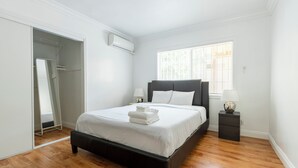 Een slaapkamer met een bed, nachtkastje, lamp en een raam met jaloezieën.
