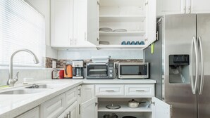 Een moderne keuken met witte kasten, een roestvrijstalen koelkast, een inbouwoven en een magnetron.