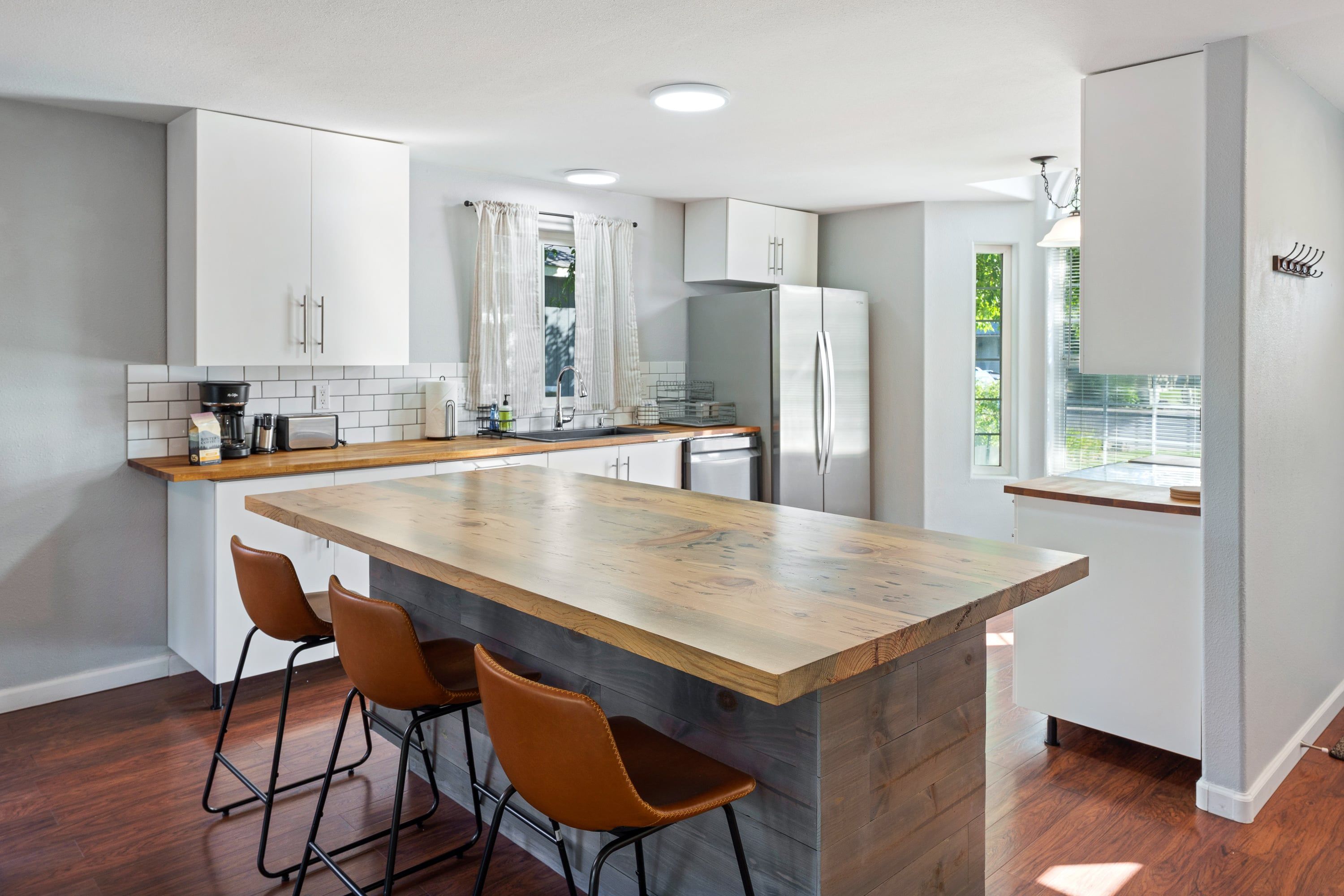 A modern kitchen with a central island, bar stools, and a refrigerator.