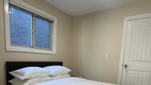A bedroom with a bed, a window, a door, and a nightstand. - Cozy 1-BR Suite in West Side • Kitchen & Living (Vancouver)
