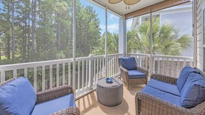 Een balkon met rieten meubels, een plafondventilator en uitzicht op een bos.