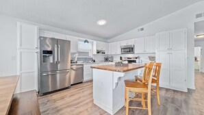 A modern kitchen with white cabinetry, stainless steel appliances, and a wooden island with seating. - Huge Private Pool | Firepit | Beach One Block Away (gulf shores)