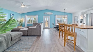 A spacious living area with a sofa, a dining table with chairs, a kitchen with a refrigerator, and a ceiling fan. - Huge Private Pool | Firepit | Beach One Block Away (gulf shores)