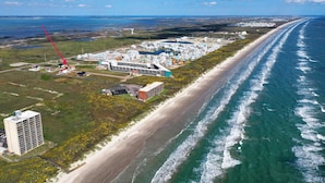 An aerial view of a coastal area with a long beach, a large cruise ship docked, and several buildings including a tall hotel. - 2 Homes, Sleeps 22 Steps to the Beach, Private Pool, Fire Pit, Balcony Views (Port Aransas)