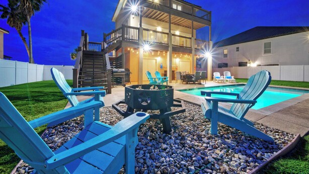A two-story house with a balcony, a pool, and outdoor seating with Adirondack chairs. - 2 Homes, Sleeps 22 Steps to the Beach, Private Pool, Fire Pit, Balcony Views (Port Aransas)