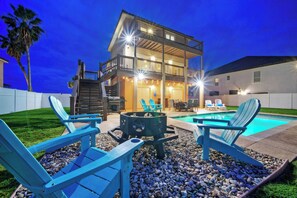 Una casa de dos pisos con balcón, piscina y mobiliario exterior con sillas tipo Adirondack.