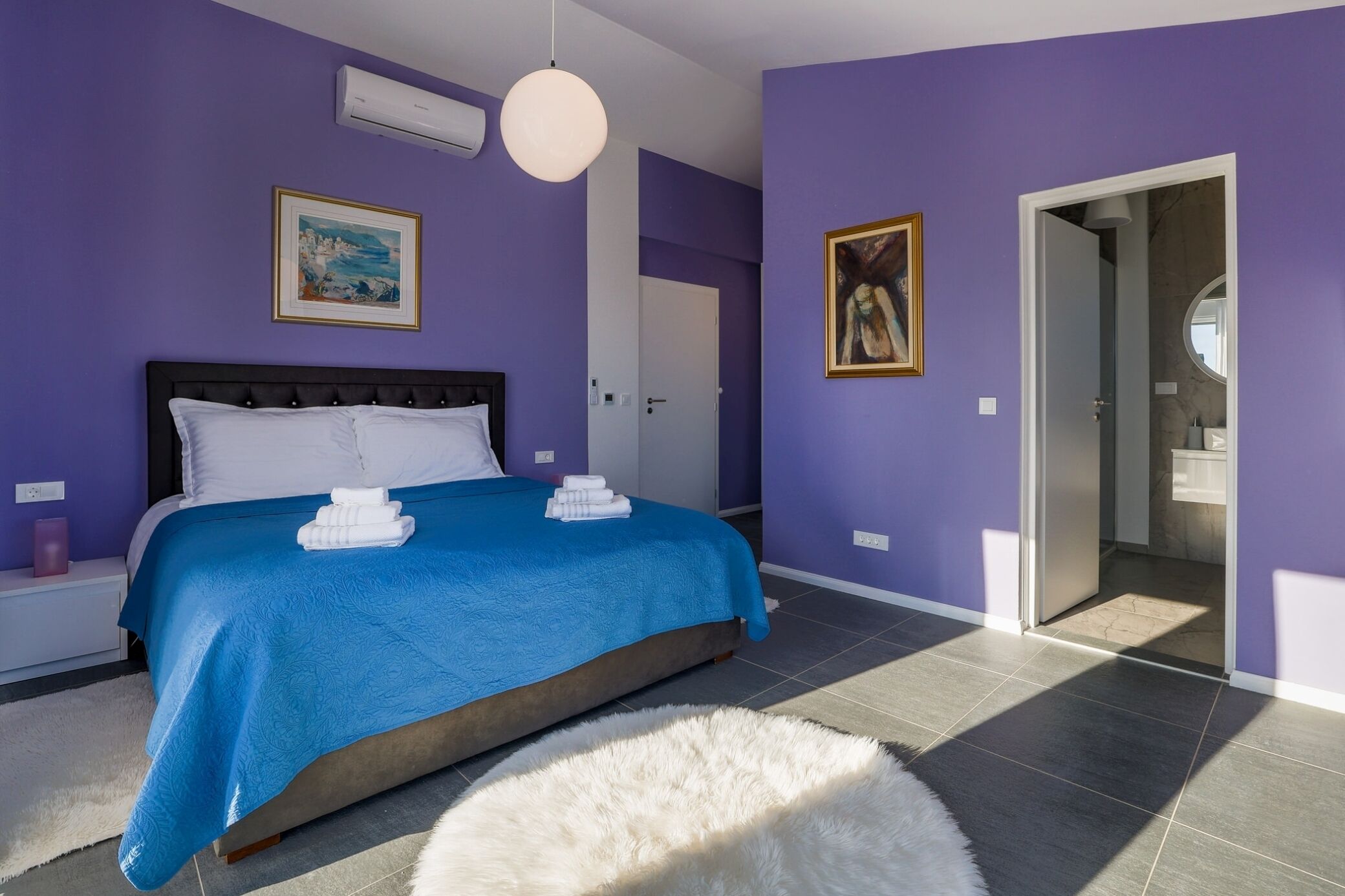 A bedroom with a bed, a white fluffy rug, and a door leading to a bathroom.