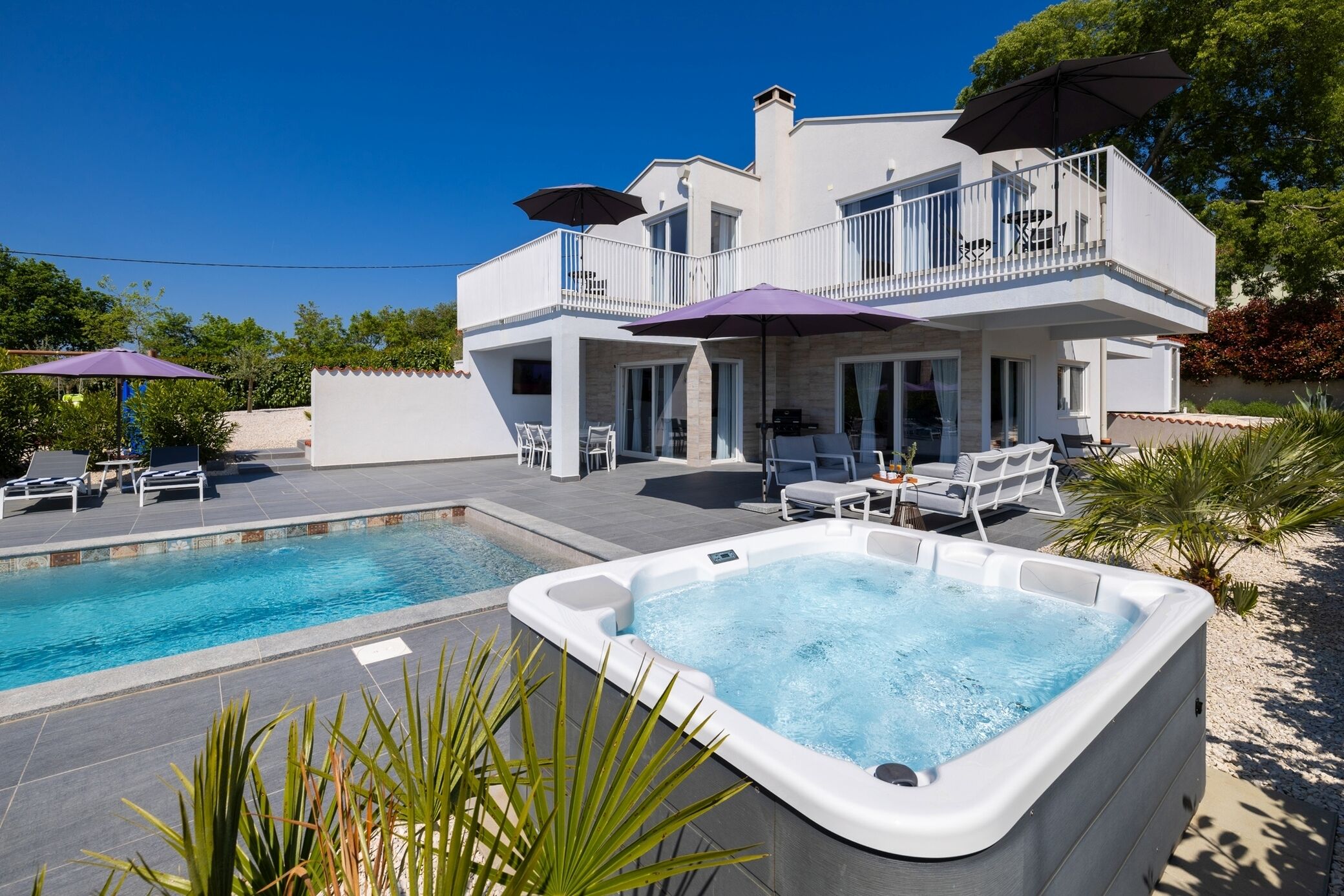 Une maison moderne à deux étages dotée d’une piscine, d’un jacuzzi extérieur et de mobilier de jardin.