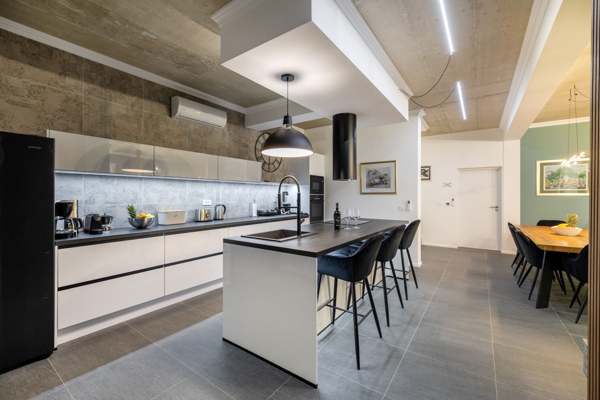 A modern kitchen with a central island, bar stools, and a dining area with a table and chairs.