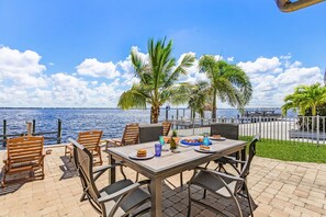Un área de comedor al aire libre con vista al mar, con una mesa dispuesta con platos, vasos y una piña.