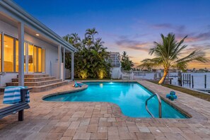 A swimming pool with a curved design, surrounded by a patio area with a bench and a covered seating area.