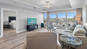 Een ruime woonkamer met een grote televisie, een bank, een glazen salontafel en een balkon met uitzicht.