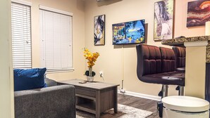 A living room with a sofa, a coffee table, a TV, and a trash can.
