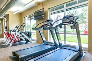Un gimnasio con cintas de correr, una bicicleta estática y un televisor en la pared.