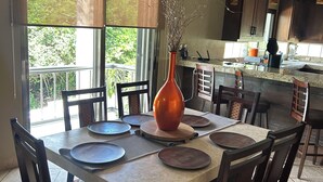 Un comedor con una mesa dispuesta para cuatro, un florero con ramas y vistas al exterior a través de amplios ventanales.