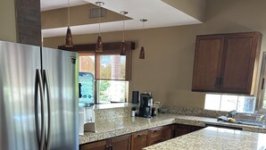 Una cocina con refrigerador de acero inoxidable, encimeras de granito, armarios de madera y un refrigerador para vinos.