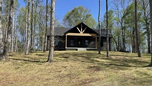 A cabin with a porch, surrounded by tall trees. - Peaceful Hilltop Lake Retreat (Lynchburg)