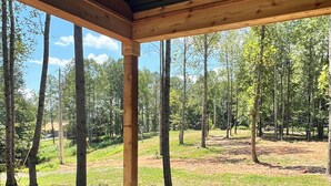 A covered outdoor area with wooden beams and a concrete floor, surrounded by trees and a grassy field. - Peaceful Hilltop Lake Retreat (Lynchburg)