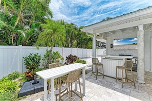 A patio with a white table and chairs, a bar area with stools, and a view of the beach. - Casa Spoonbill in Bradenton, FL (Bradenton)