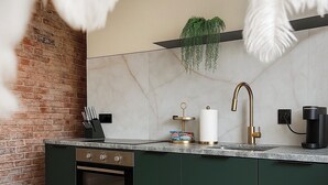 A kitchen with a brick wall, a marble backsplash, a green cabinet, a sink with a gold faucet, and a coffee machine.