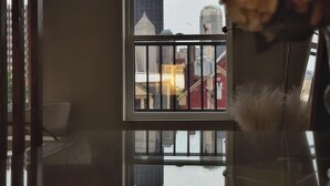 A room with a view through a window, a vase with dried flowers, and a reflection on the glass surface.