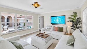 Een ruime woonkamer met een groot raam, een aan de muur bevestigde televisie en een gezellige zithoek met een bijzettafeltje.