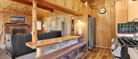 L’intérieur d’une cabane en bois comprend un coin repas, une cheminée, un réfrigérateur et une cuisinière.