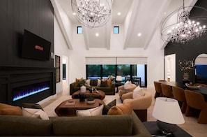 Uma sala de estar moderna com lareira, sofás, televisão e um candelabro.