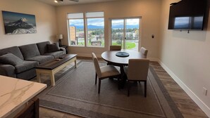 A living room with a sofa, coffee table, TV, and a dining area with chairs and a table. - Heart of Homer - Redoubt (Homer)