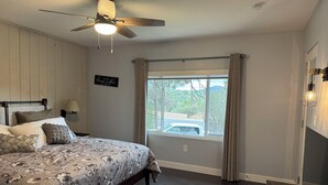 A bedroom with a bed, a ceiling fan, a window with curtains, a nightstand, and a wall-mounted lamp. - Vintage Charm, Modern Comfort & Private Casita. Near Downtown Prescott. (Prescott)