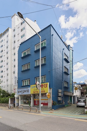 Um edifício de vários andares com fachada azul, uma vitrine visível com sinalização e uma bicicleta estacionada na frente.