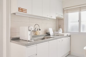 Una cucina moderna con mobili bianchi, forno integrato, lavello e finestra con persiane.