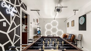 Una habitación con una mesa de fútbol de mesa, un dardo y un letrero de neón.
