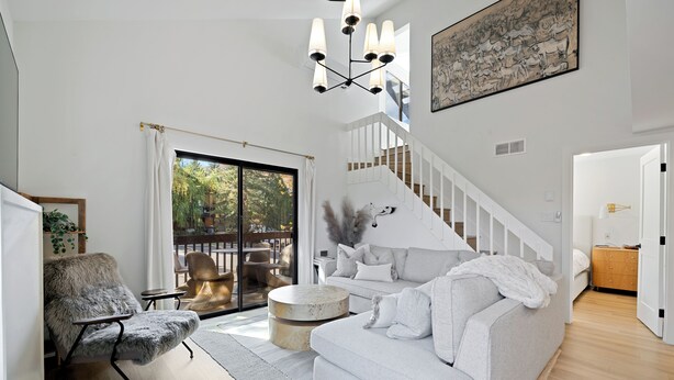 A modern living room with a white sofa, a furry armchair, a round coffee table, and a staircase leading to another level.