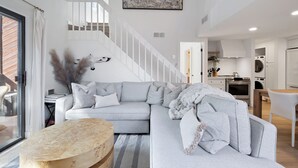 A modern living room with a grey sectional sofa, a wooden coffee table, and a staircase leading to a kitchen area.