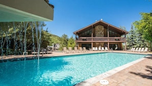 A pool area with a wooden deck, lounge chairs, and a building with a balcony.