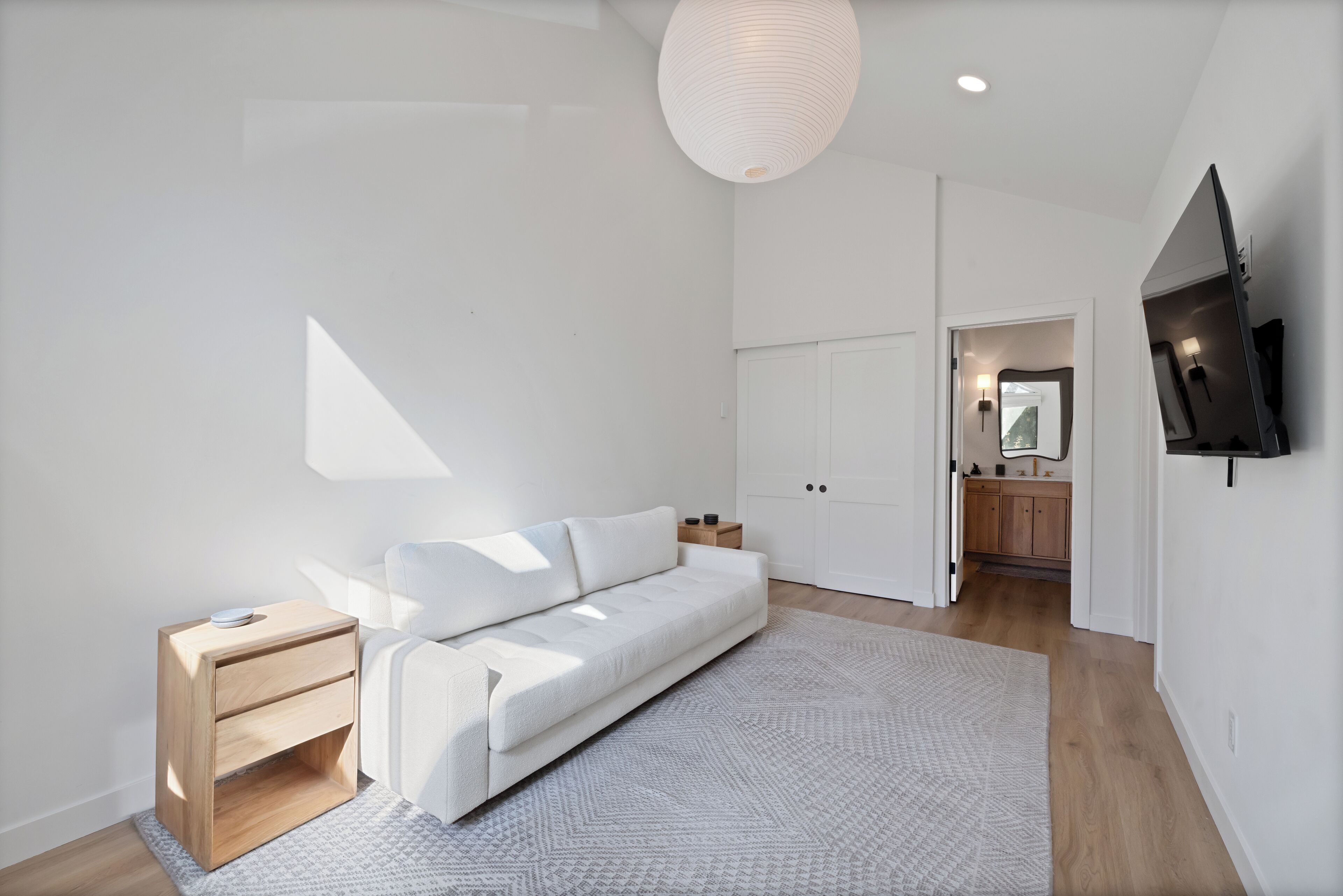 A modern living room with a white sofa, a small wooden side table, and a patterned rug.