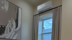 Ein modernes Schlafzimmer mit einem Bett, einer Wand-Klimaanlage, einem mit Vorhängen ausgestatteten Fenster und einer dekorativen Lampe.