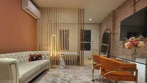 Ein modernes Zimmer mit einem weißen Sofa, einem Glastisch mit orangefarbenen Stühlen, einer Ziegelwand und einem großen Spiegel.