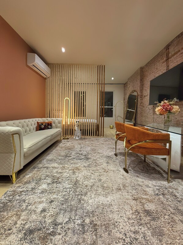 Ein modernes Zimmer mit einem weißen Sofa, einem Glastisch mit orangefarbenen Stühlen, einer Ziegelwand und einem großen Spiegel.