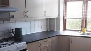 A kitchen with white cabinets, a stove, and a window with blinds.
