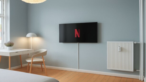 A modern bedroom with a bed, a desk, a chair, a TV mounted on the wall, and a radiator.