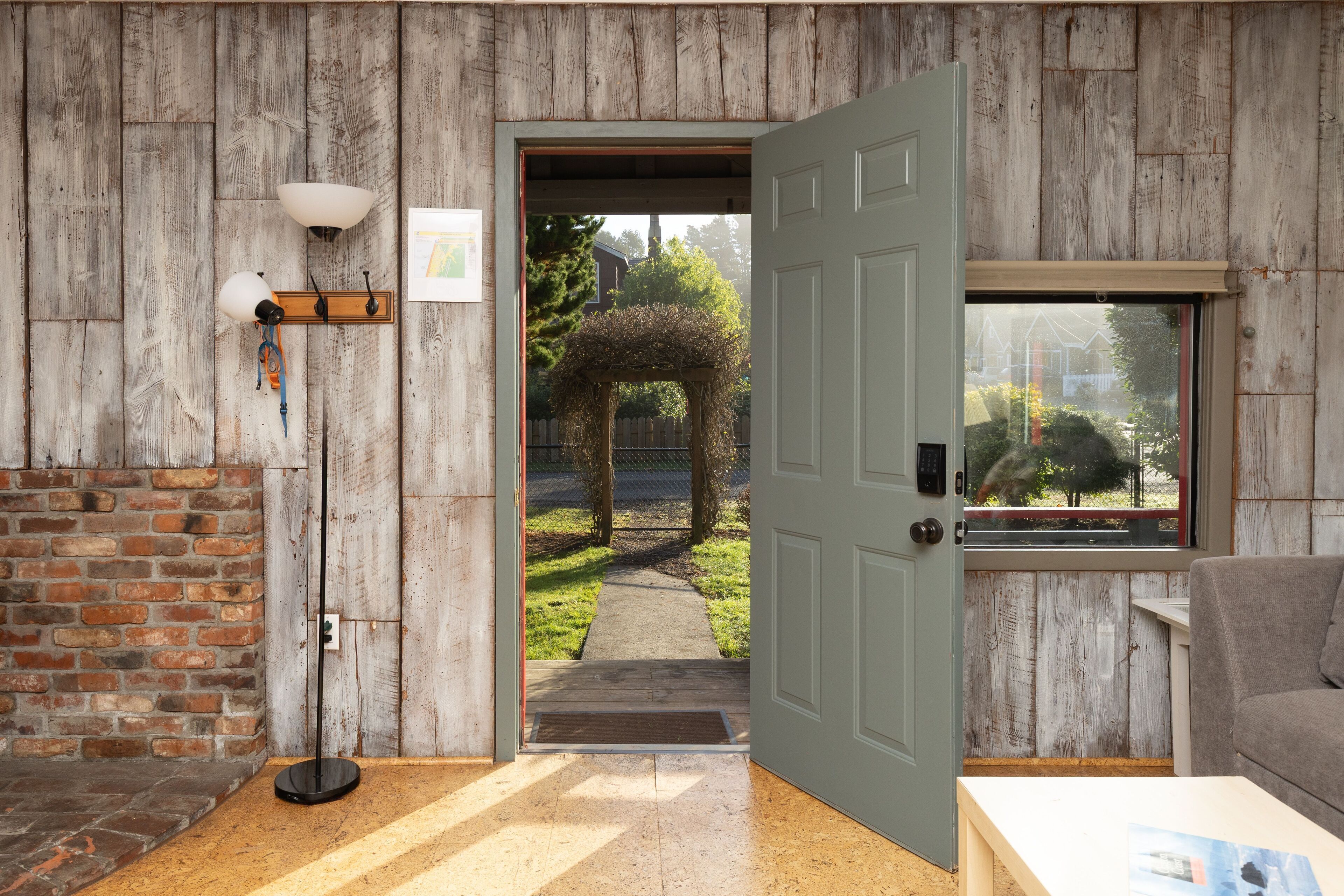 A room with a wooden wall, a door leading outside, a floor lamp, and a window.