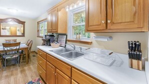 A kitchen with wooden cabinets, a double sink, and a dining area with chairs and a table. - Lookout Mtn. Escape w/ Fire Pit & 1 Acre Level Lawn- Mins to Cloudland Canyon (Rising Fawn)