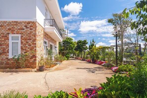 Un edificio residencial con fachada de ladrillo, un balcón y un jardín con diversas plantas y flores.