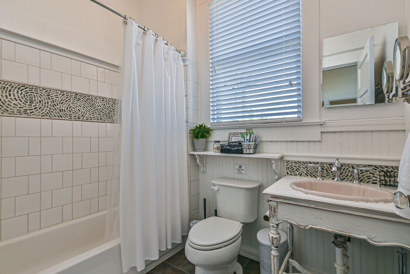 Une salle de bain équipée d’une baignoire, de toilettes, d’un lavabo et d’une fenêtre avec des stores.