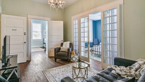 A spacious living room with a leather sofa, a glass coffee table, and a chandelier. There are two doors leading to other rooms, one labeled "Ruby". - 3 Room 2nd-Floor Suite near Beach, Pier, Strand (Galveston)