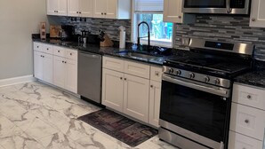 A modern kitchen with white cabinets, stainless steel appliances, and a marble floor.
